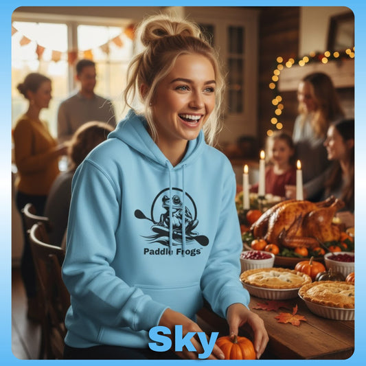 Blonde lady at Thanksgiving wearing Sky blue | Paddle Frogs™ Soft Fleece Hoodie: Soft Fleece, Wild Soul (12 Colors) Woman wearing a blue hoodie with 'Paddle Flogs' design, standing in a festive indoor setting with people and food.