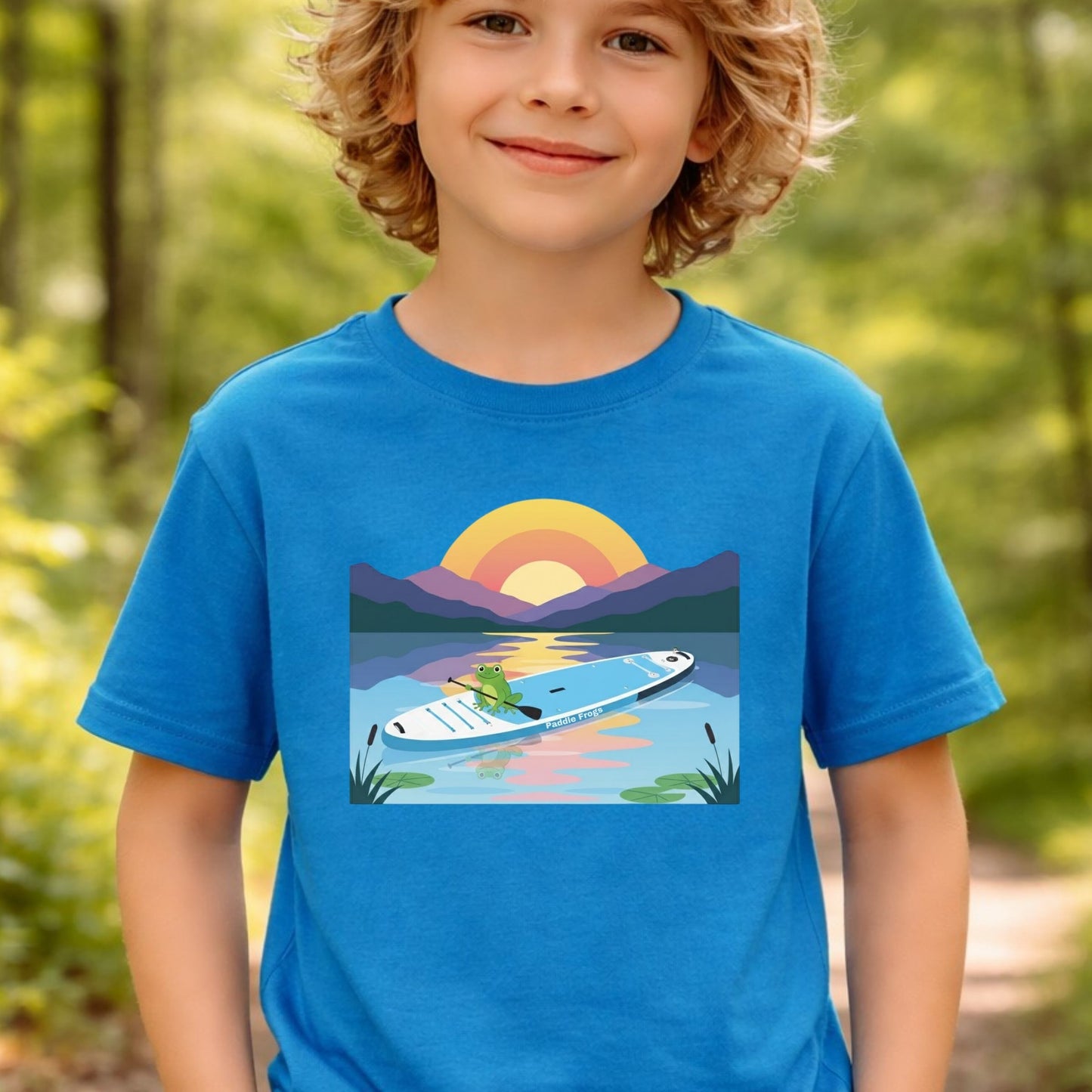 Child wearing a Sapphire blue Paddle Frogs t-shirt with a graphic of a paddleboard on a lake