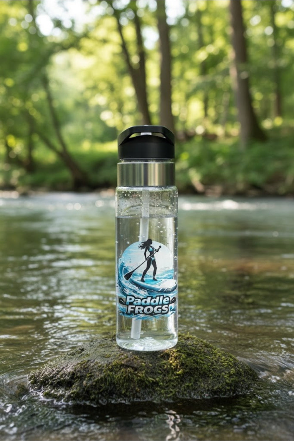 Clear water bottle with Paddle Frogs Lady of the Current paddleboard design on a rock by a river
