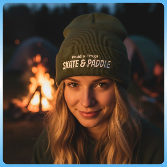 Woman wearing a 'Paddle Frogs Skate & Paddle' beanie in front of a campfire. Olive Green embroidered