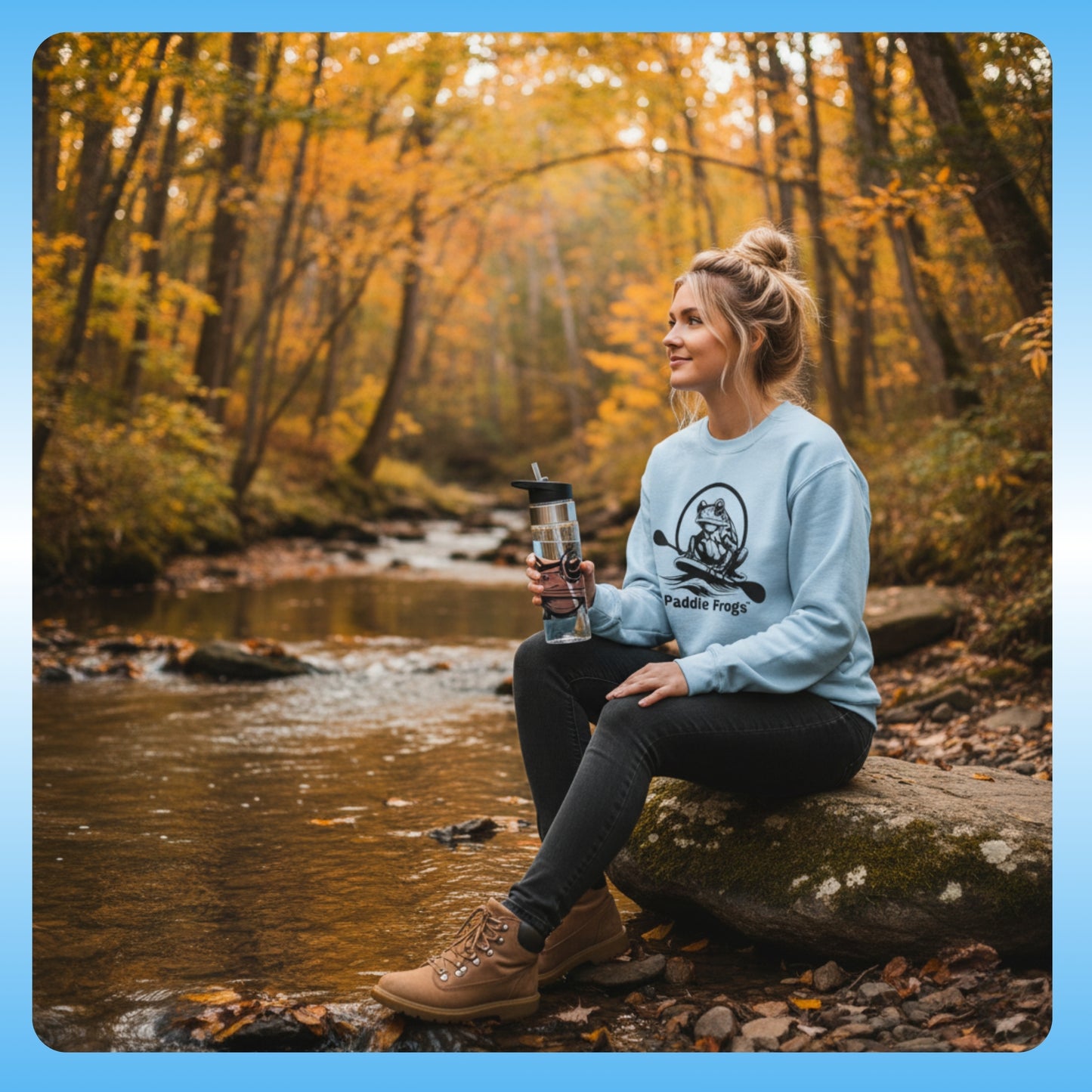 and crystal clear water bottle | Paddle Frogs™ Sweatshirt light blue | Woman sitting by a stream in a forest during autumn, holding a water bottle.