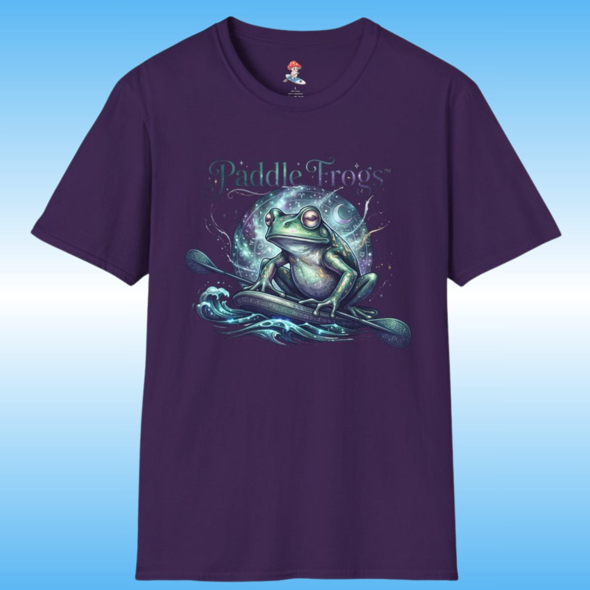 A dark purple short-sleeve t-shirt with a graphic of a green frog on a paddle board boat on stylized water waves, with the text 'Paddle Frogs' above it. The shirt is displayed against a blue gradient background.