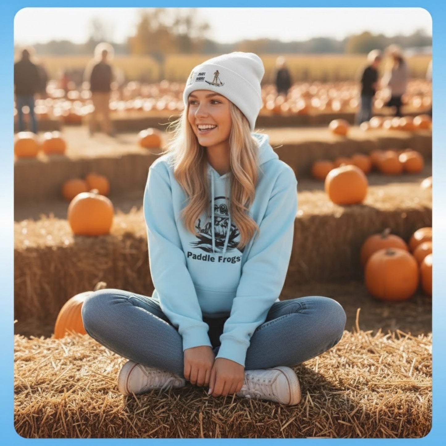 Tides & Trails Beanie: Life in Balance, Skate & Paddle Woman sitting crisscross applesauce on hay bales at a pumpkin patch wearing a light blue hoodie and white beanie.