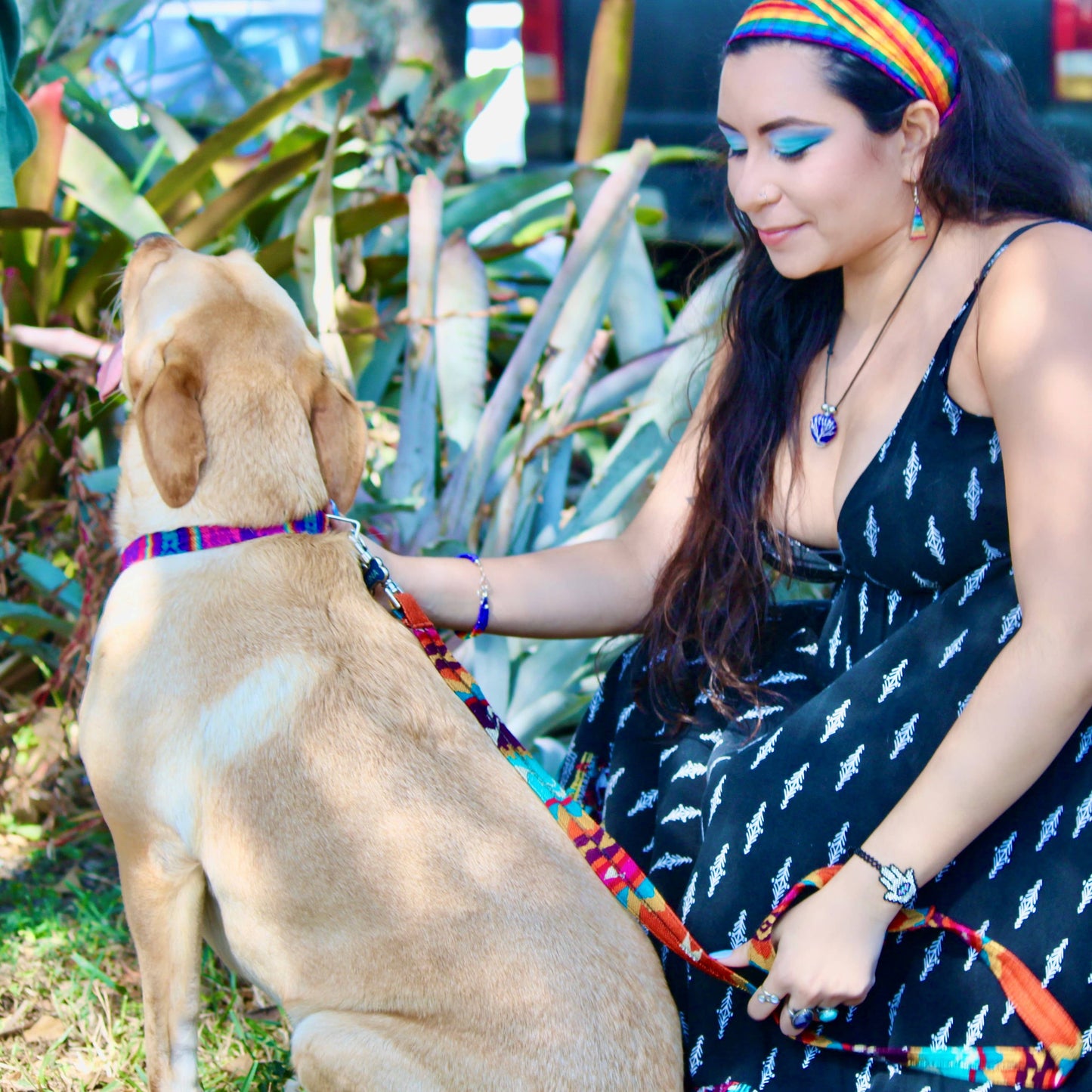 Woman in a black dress with white patterns sitting next to a dog in a garden setting