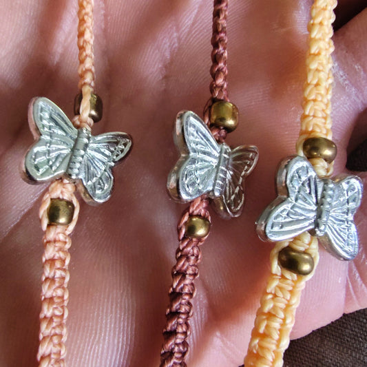 Three butterfly-themed friendship bracelets with different colored cords on a hand.