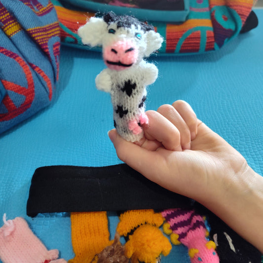Hand holding a small knitted cow finger Puppet toy with colorful fabric background