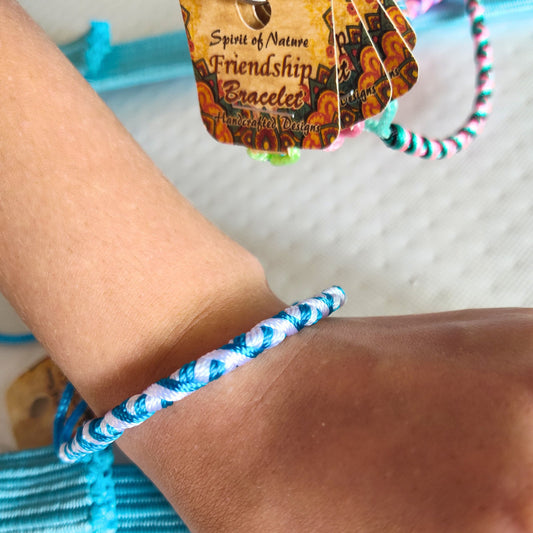 Colorful blue braided BFF bracelet on a wrist with 'Spirit of Nature Friendship Bracelets' packaging in the background.