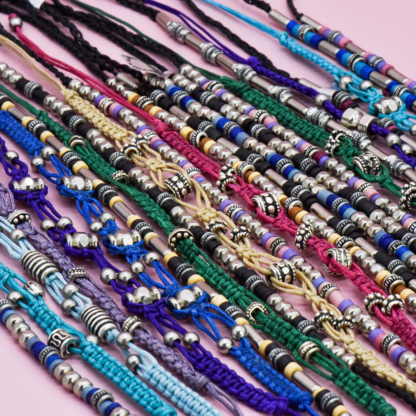 Collection of colorful bracelets with metal beads on a pink background