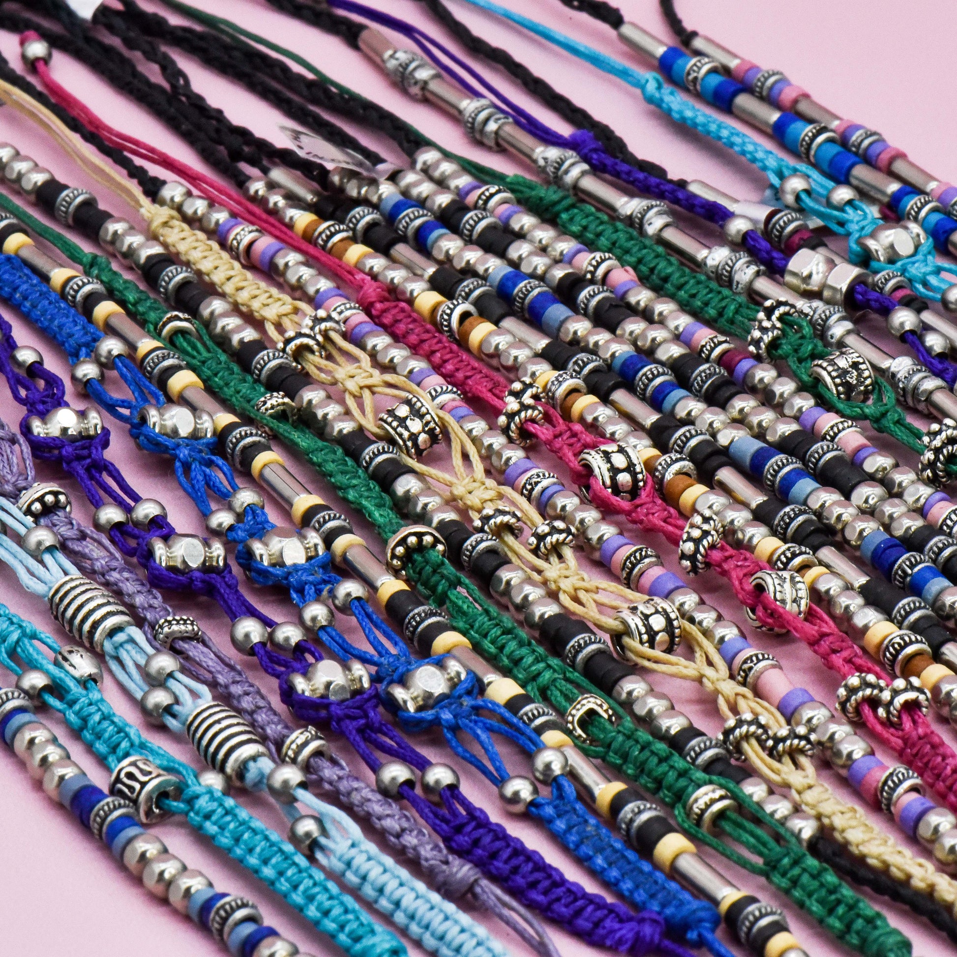 Collection of colorful bracelets with metal beads on a pink background