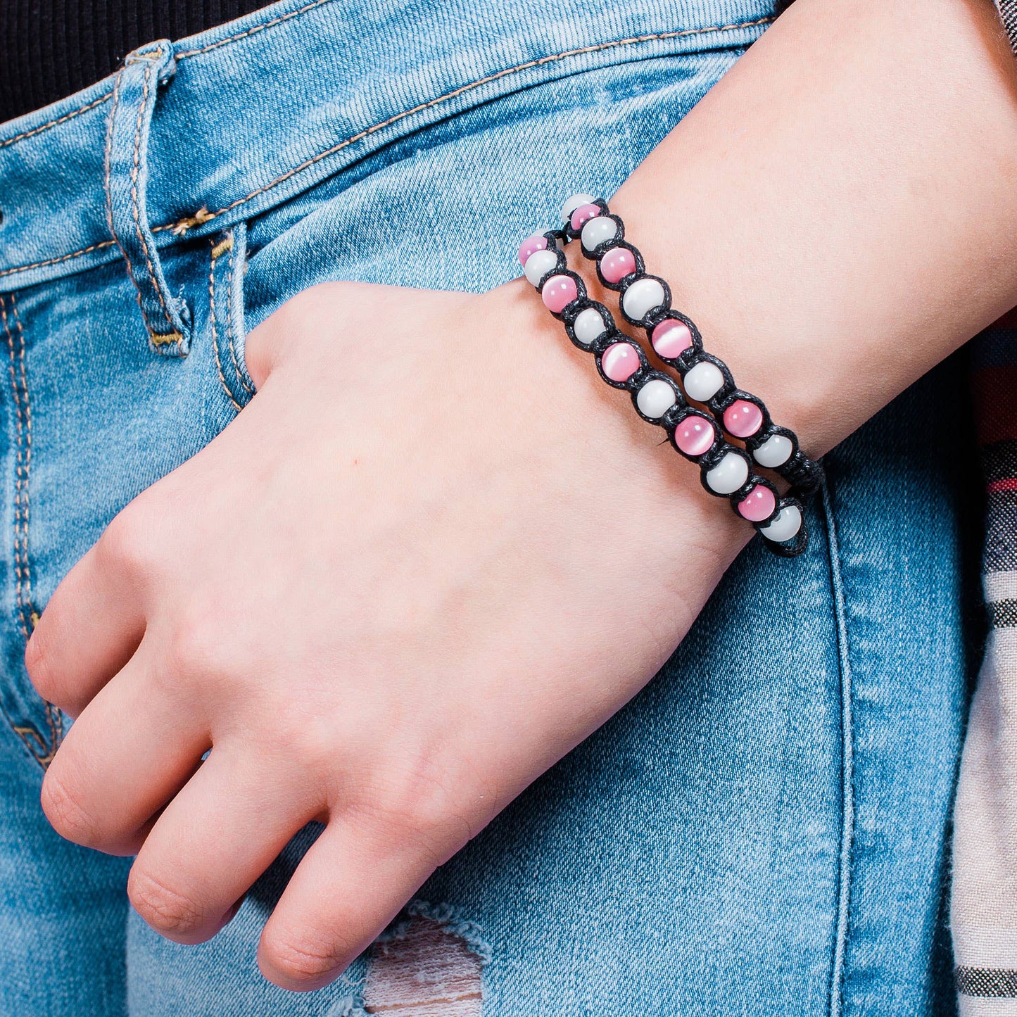 Close-up of a hand wearing a cat's eye beaded bracelet on a denim background