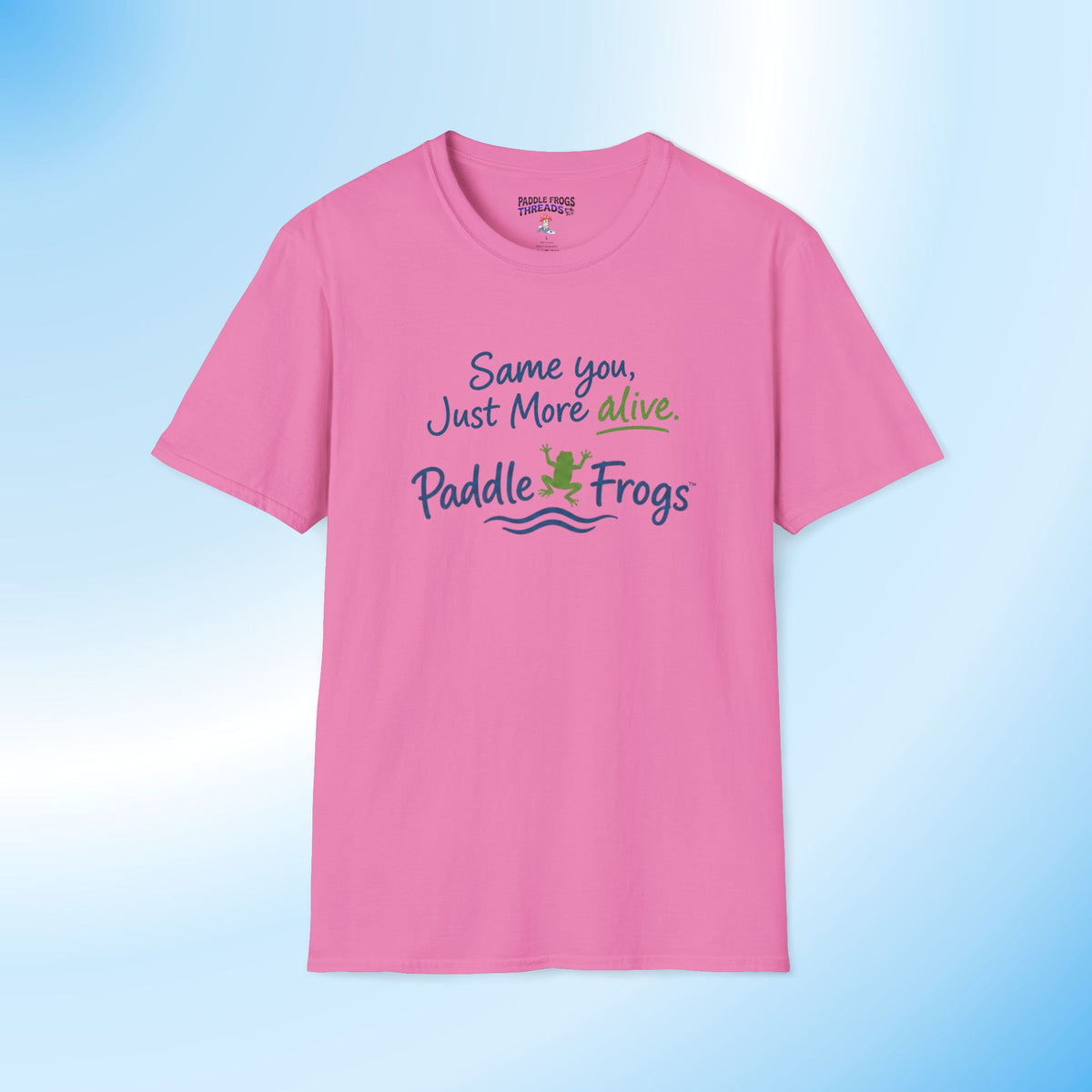 A pink short-sleeve crewneck t-shirt with a graphic on the chest that reads 'Same you, Just More alive. Paddle Frogs' in blue, green, and white text, accompanied by a small frog illustration and wavy lines.