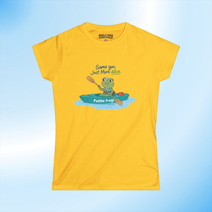 A yellow short-sleeve t-shirt with a cartoon graphic of a green frog paddling in a teal kayak, accompanied by the text 'Same you Just More Alone' and 'Paddle Frog!'. The shirt is displayed flat against a light blue gradient background.