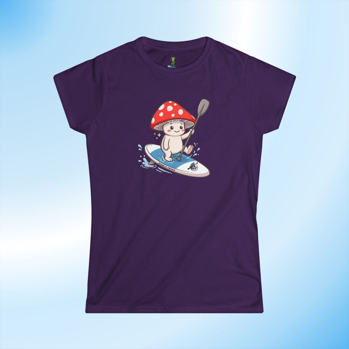 A women's short-sleeve t-shirt in deep purple, featuring a cartoon graphic of a white mushroom Shiro paddling on a blue paddleboard. The t-shirt is displayed against a light blue gradient background.