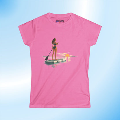 An Azalea pink short-sleeve ladies crewneck t-shirt featuring a graphic print of a woman paddleboarding on a lake at sunset. The brand name 'Paddle Frogs' is printed inside the collar.