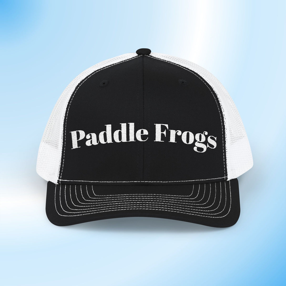 A black and white trucker hat with 'Paddle Frogs' printed in white text on the front panel, set against a light blue gradient background.