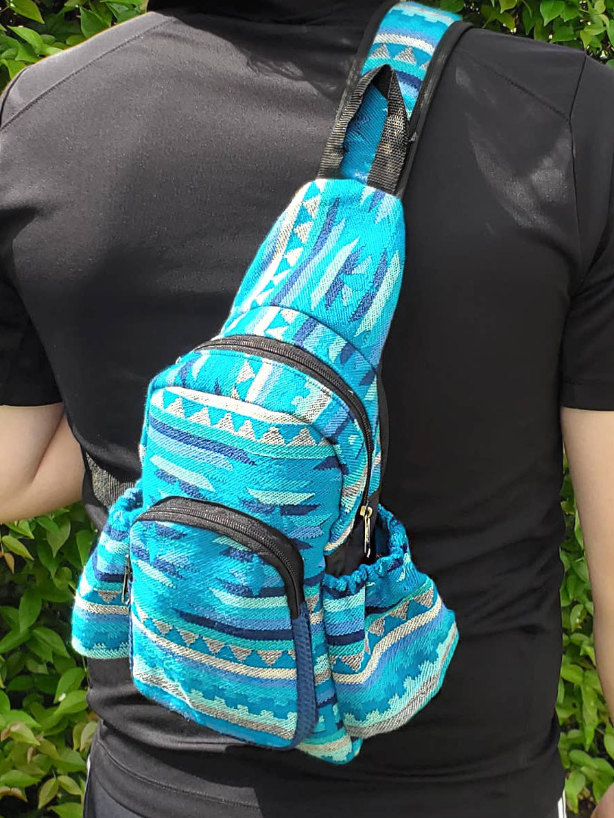 Person wearing a blue patterned sling bag against a green hedge background