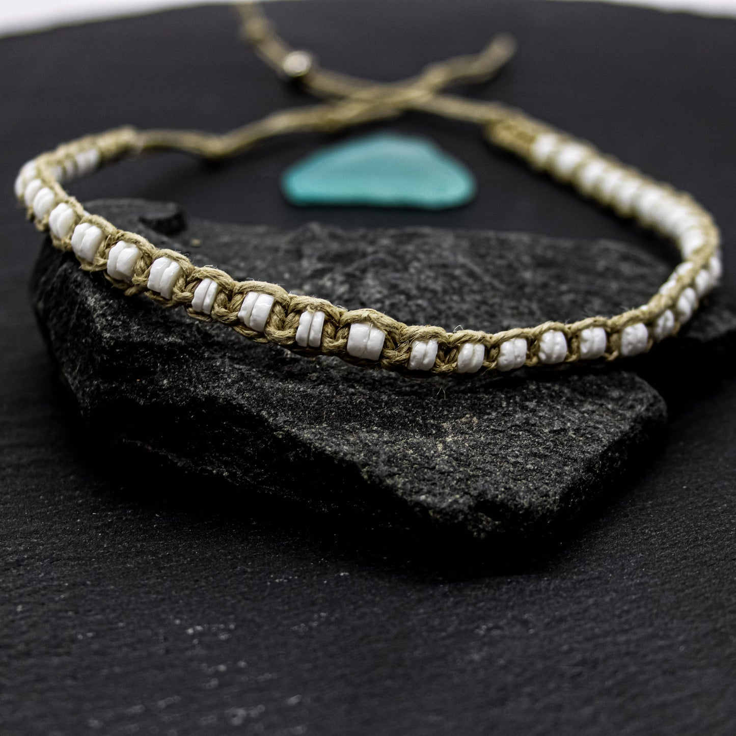 Bracelet with white puka shell beads and hemp thread on a dark stone surface