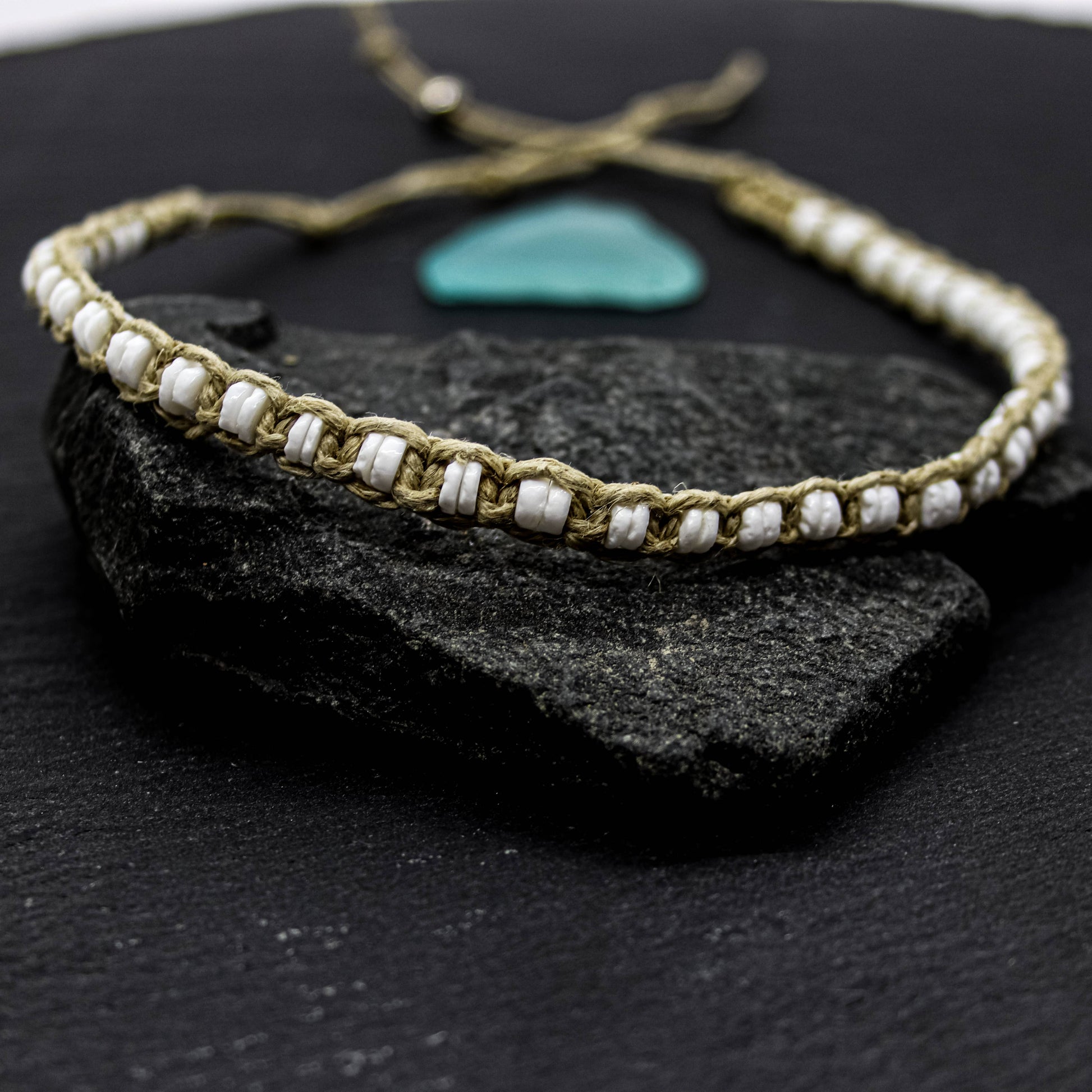 Bracelet with white puka shell beads and hemp thread on a dark stone surface