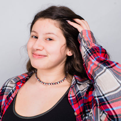 Person wearing a plaid shirt with a  cat's eye necklace neutral background