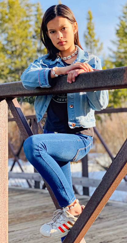 Person wearing a denim jacket and jeans sitting on a wooden deck with trees in the background