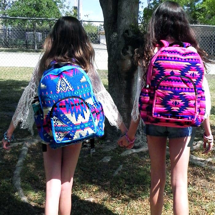 Two girls wearing colorful patterned backpacks walking outdoors.