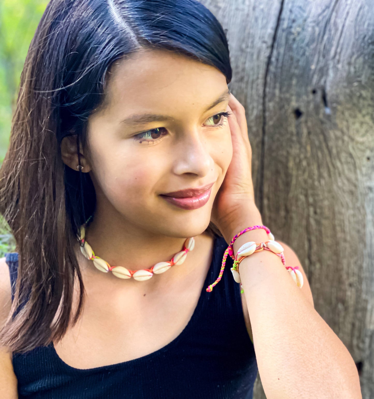 Young girl wearing a shell necklace and bracelets, leaning against a wooden surface.