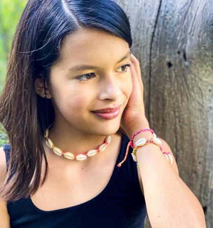 Young girl wearing a shell necklace and bracelets, leaning against a wooden surface.