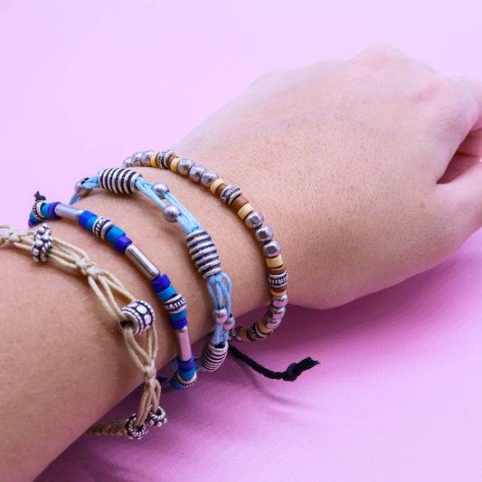 Close-up of a wrist wearing multiple colorful beaded bracelets on a pink background