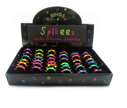 A display box of Spikeez Spiky Silicone Jewelry rings on a white background. The black display box features a sign reading 'Spikeez Spiky Silicone Jewelry' and is filled with multiple neon-colored spiky rings in pink, green, yellow, and blue.