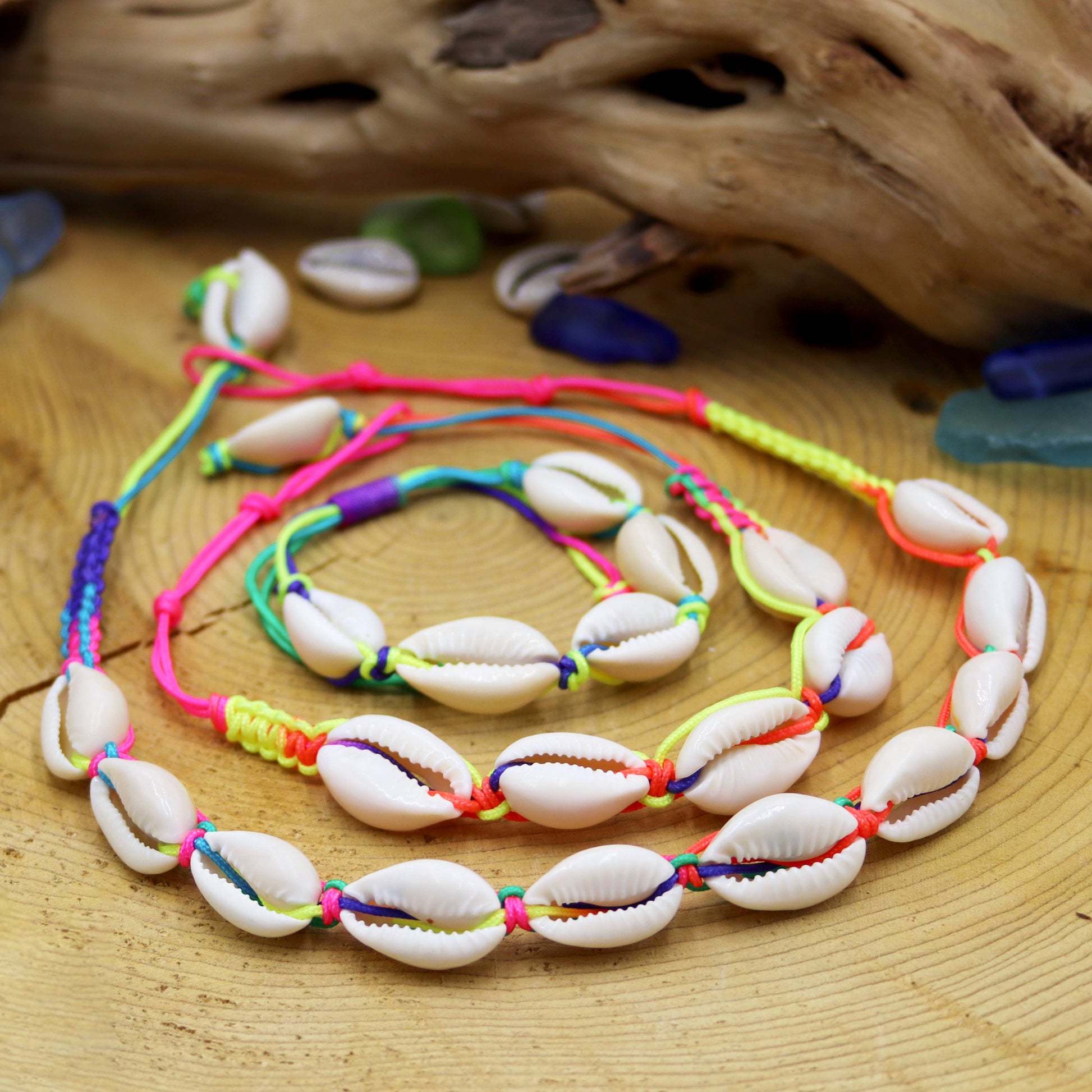 Colorful shell necklace on a wooden surface with shells and driftwood.