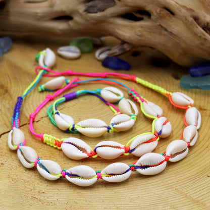 Colorful shell necklace on a wooden surface with shells and driftwood.