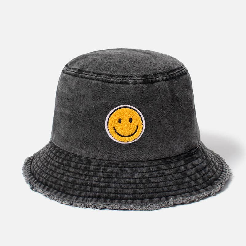 A dark gray washed bucket hat featuring a yellow smiley face patch on the front, set against a plain light gray background.