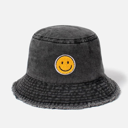 A dark gray washed bucket hat featuring a yellow smiley face patch on the front, set against a plain light gray background.