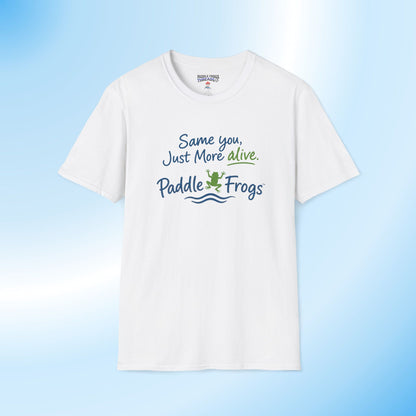 A white short-sleeve crewneck t-shirt with a graphic printed on the chest that reads 'Same you, Just More alive. Paddle Frogs' in blue and green lettering with a small frog illustration, displayed against a light blue gradient background.