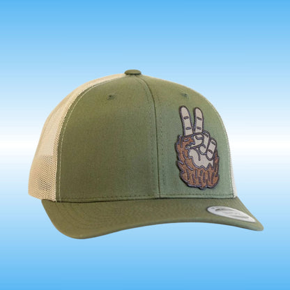 An olive green trucker cap with beige mesh back panels and a graphic patch of the hand of bigfoot making a peace sign on the front, set against a plain white background.