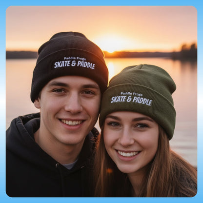 Two people wearing 'Paddle Frogs Skate & Paddle' beanies with a sunset over water background. black and olive green 