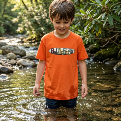 A young boy playing in a creek wearing an orange t-shirt by Paddle Frogs Kids. Claymation SUP paddleboarding tee.