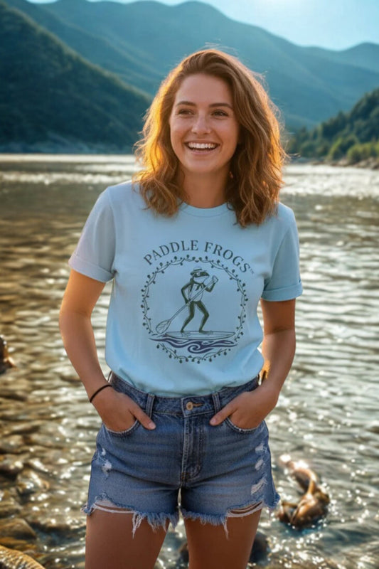 Woman wearing Country Paddler a 'Paddle Frogs' t-shirt by a lake with mountains in the background