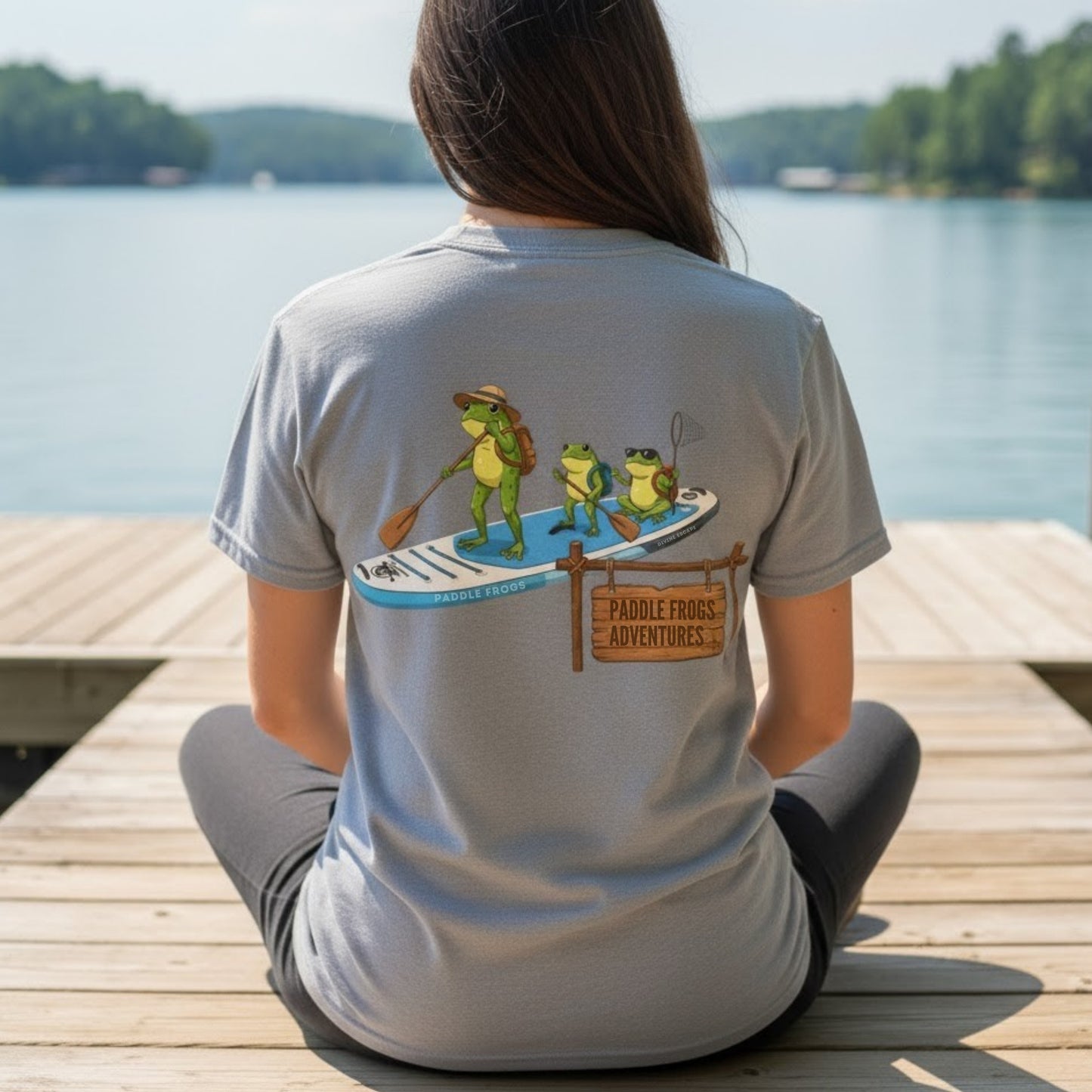 Person wearing a Paddle Frogs Adventures t-shirt with a paddleboard and frog graphic on a dock by Norris lake