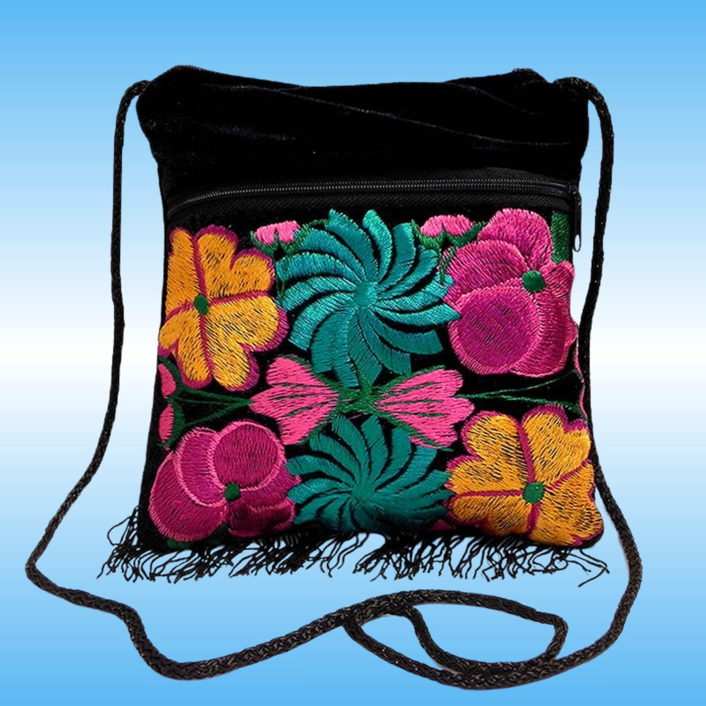 Black velvet drawstring shoulder bag with colorful floral embroidery in pink, yellow, and teal on the front pocket, finished with black fringe and a black shoulder strap, shown against a blue gradient background.