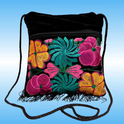 Black velvet drawstring shoulder bag with colorful floral embroidery in pink, yellow, and teal on the front pocket, finished with black fringe and a black shoulder strap, shown against a blue gradient background.