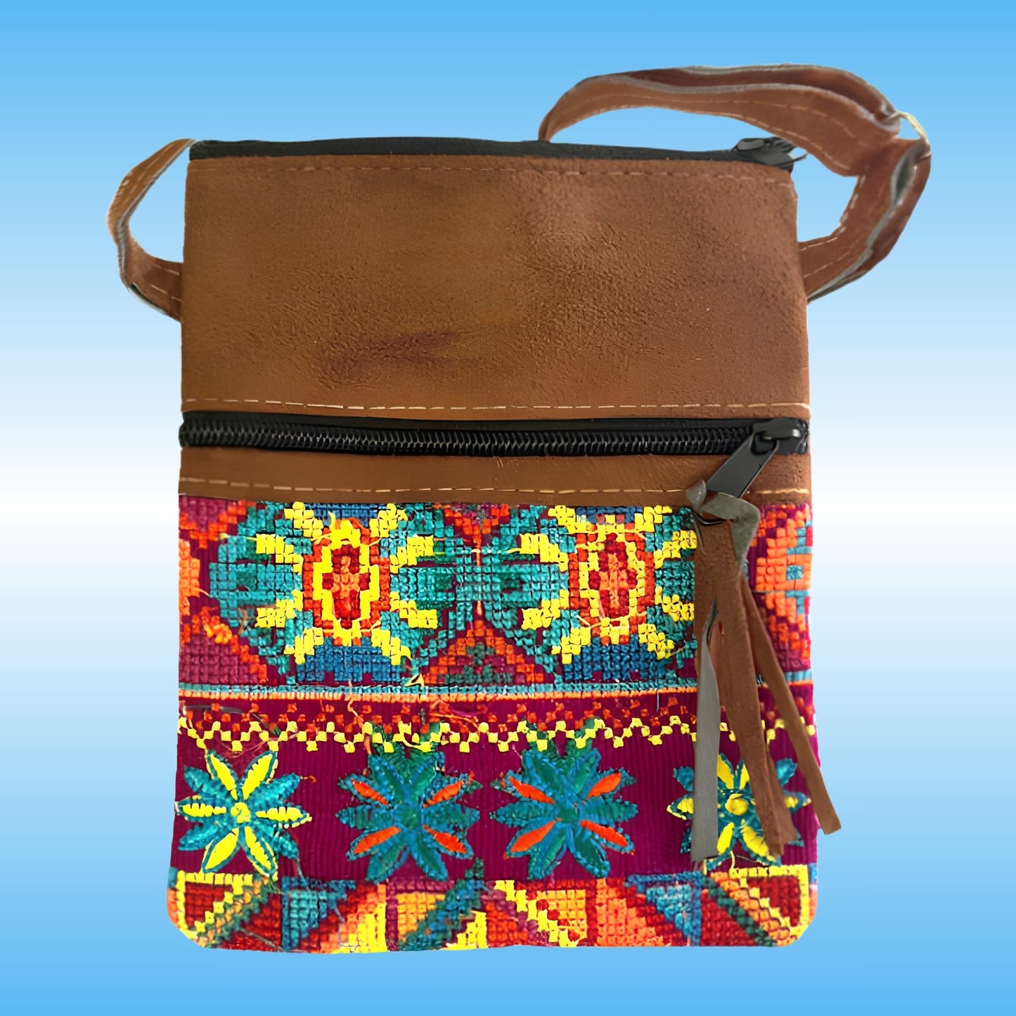 A small crossbody bag with a brown faux-leather top section and a colorful geometric embroidered pattern in red, yellow, blue, and green on the lower half, shown against a light blue gradient background.