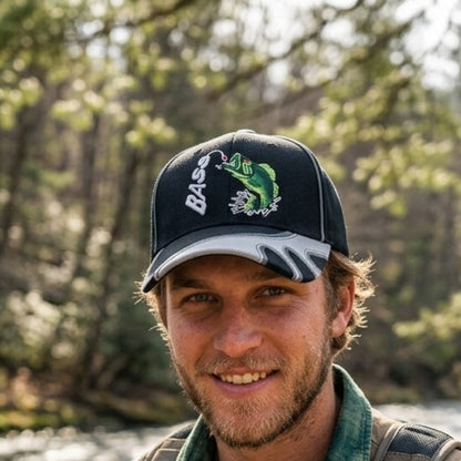 A smiling man outdoors wearing a black baseball cap with a green fish graphic and the word 'BASS' on the front, along with a green collared shirt and backpack straps visible.