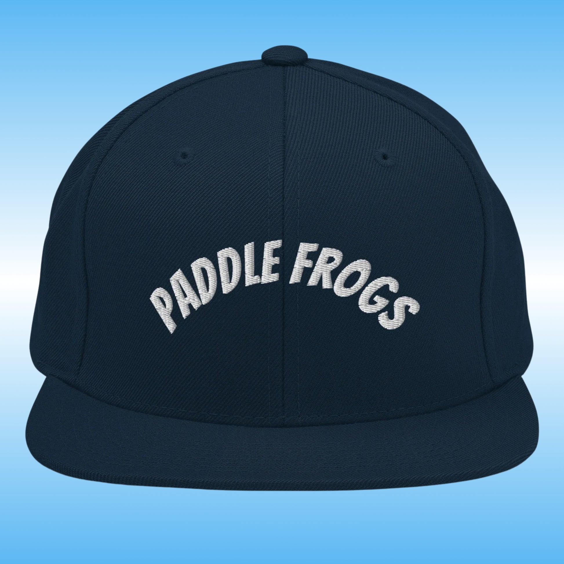 A dark navy blue flat-brim cap with 'PADDLE FROGS' embroidered in white arched text across the front, set against a light blue gradient background.