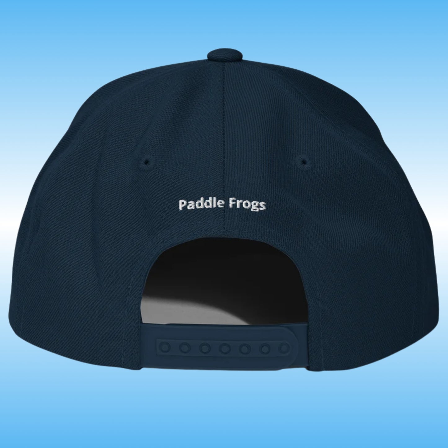 The back of a dark navy blue baseball cap with 'Paddle Frogs' embroidered in white on the crown, set against a light blue gradient background.