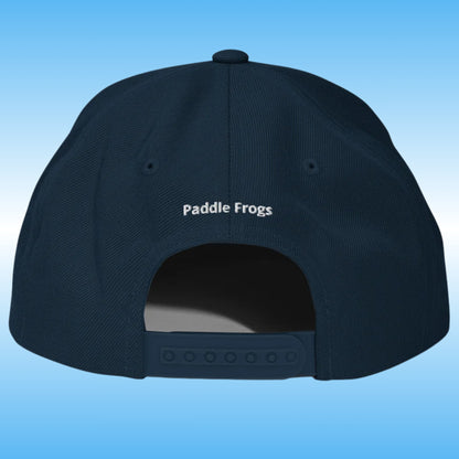 The back of a dark navy blue baseball cap with 'Paddle Frogs' embroidered in white on the crown, set against a light blue gradient background.