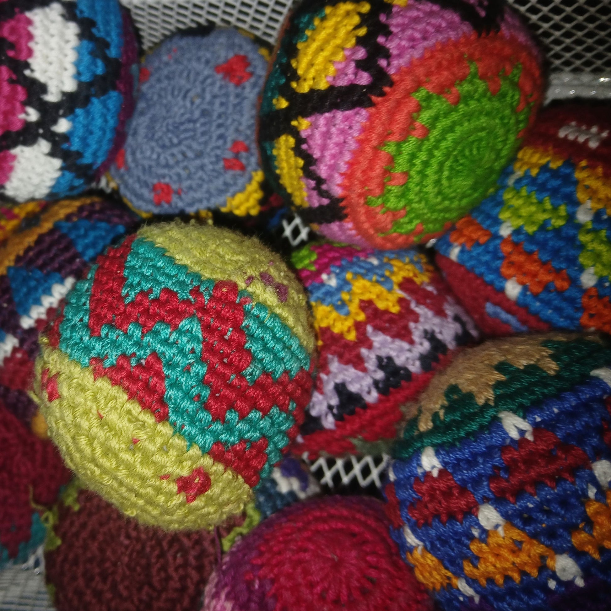A pile of colorful crocheted footbags with intricate geometric patterns in red, yellow, green, blue, pink, and white.