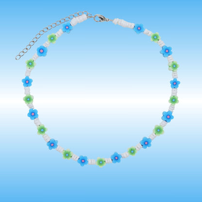 A beaded necklace with alternating blue and green flower beads, white spacer beads, and a silver-tone chain clasp, shown on a light blue gradient background.