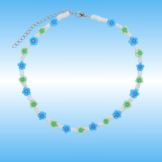 A beaded necklace with alternating blue and green flower beads, white spacer beads, and a silver-tone chain clasp, shown on a light blue gradient background.