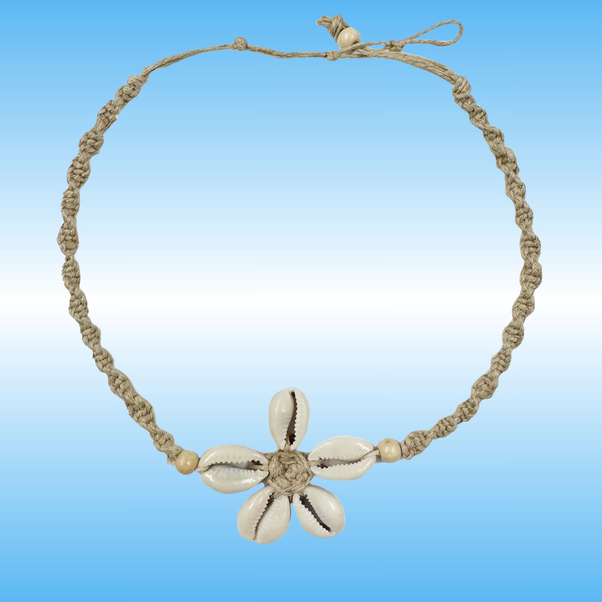 A handmade braided hemp necklace with a central flower charm made from five cowrie shells, set against a blue gradient background.